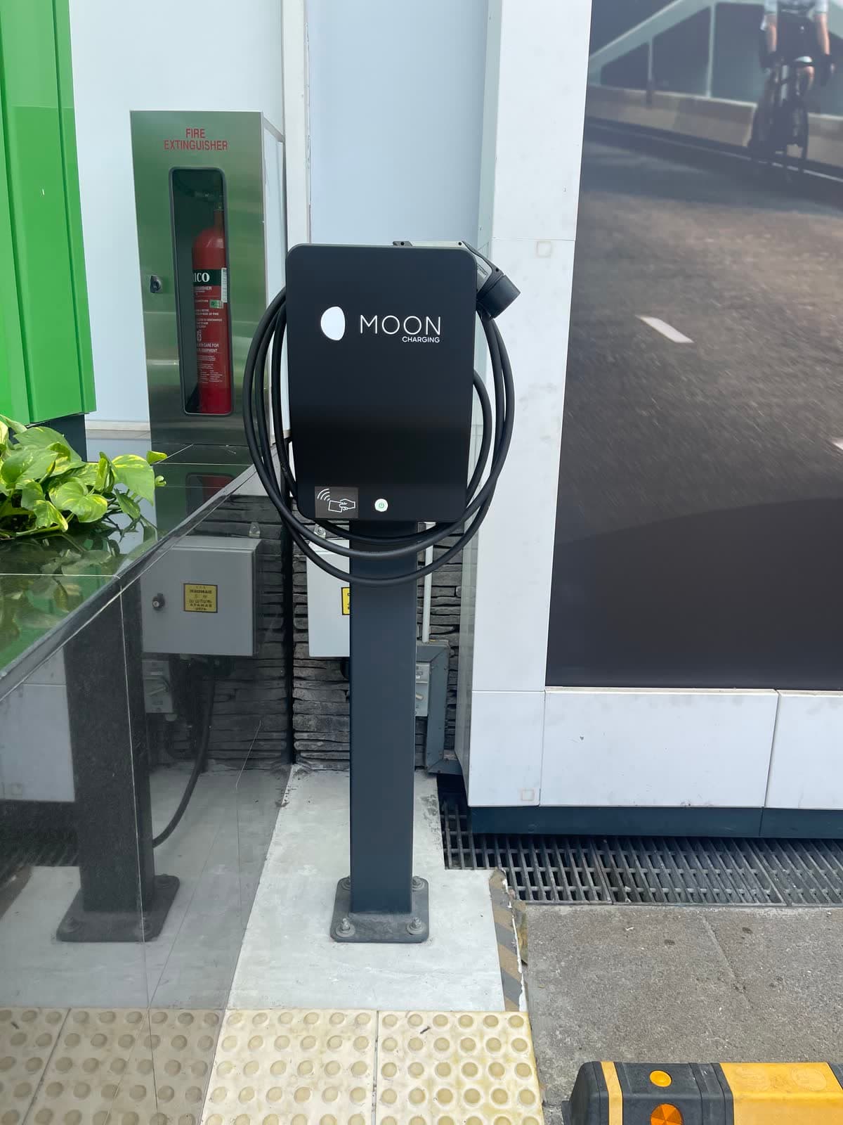 Pedestal AC charger with a holstered cable outside a building entrance
