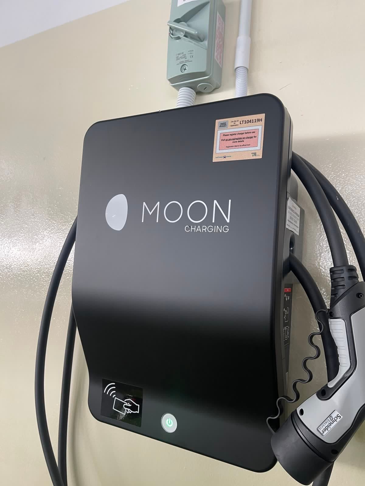 Close-up of a wall-mounted AC charger with an LTA registration label and a Type 2 plug in its holster