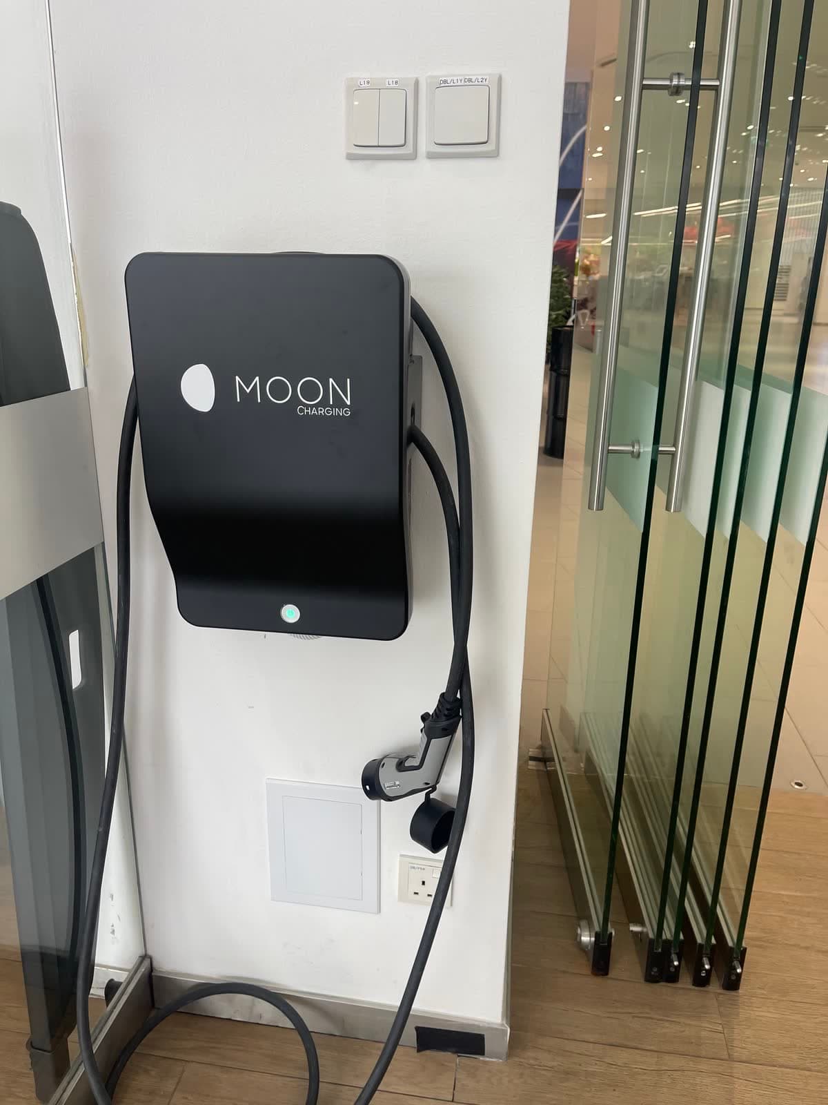 Wall-mounted AC charger beside glass doors in a commercial building, with its cable and Type 2 plug