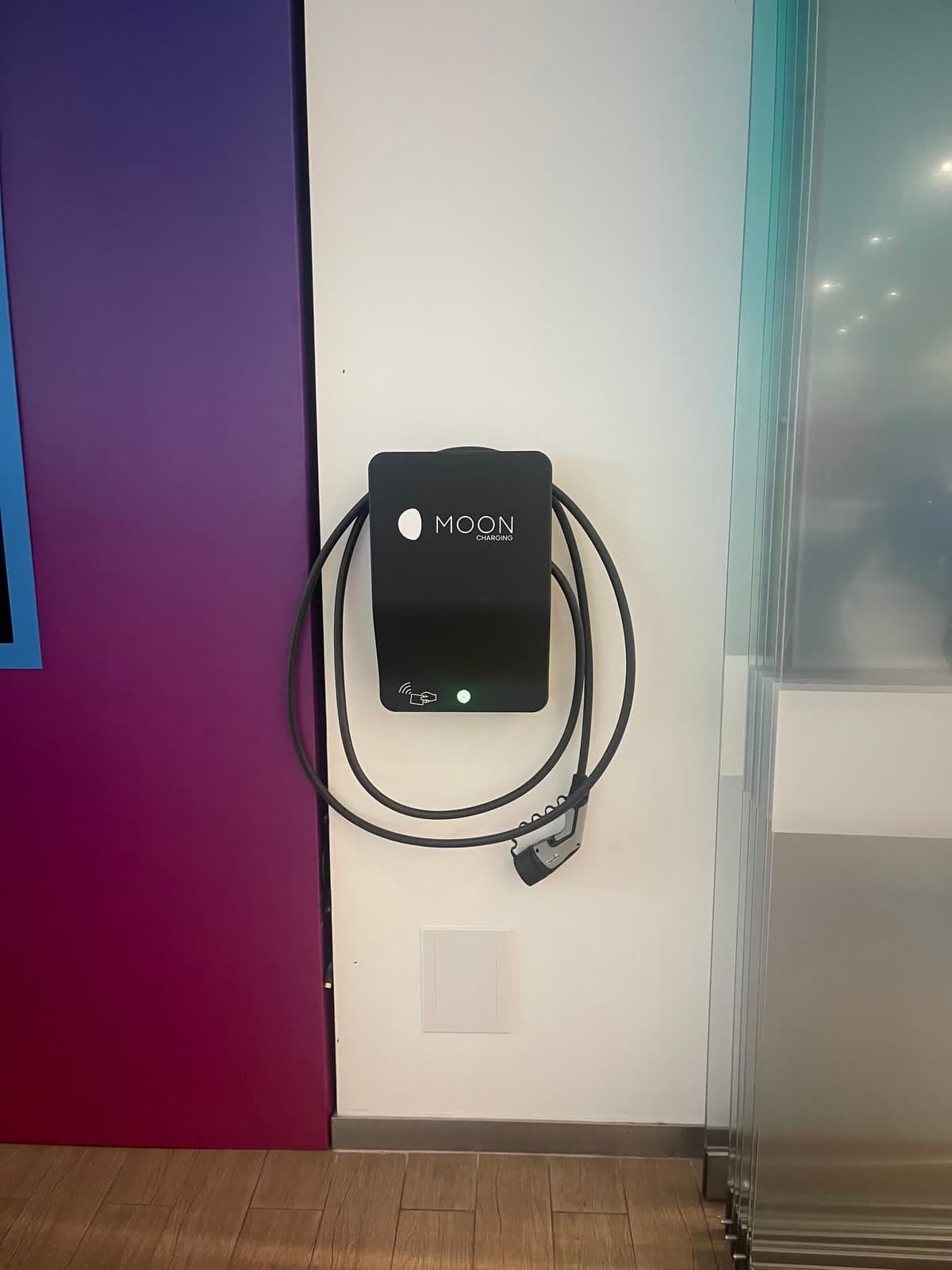Wall-mounted AC charger with a coiled tethered cable in a commercial building lobby