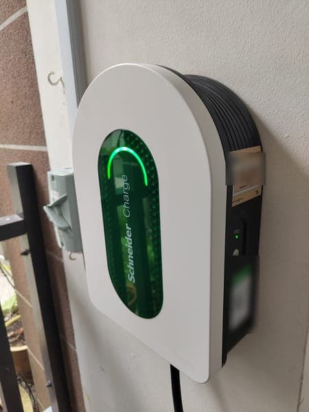White Schneider Charge wallbox with a green light panel beside a gate in a landed-home porch