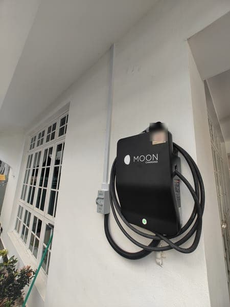 Black Moon Charging wallbox and isolator on the porch wall of a landed home with white French windows