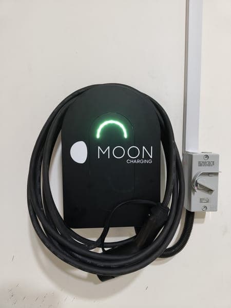 Moon Charging wallbox with a green light and a neatly coiled cable beside its isolator