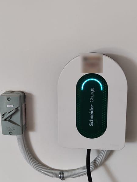 White Schneider Charge wallbox with a green light panel and isolator, its cable run in grey conduit