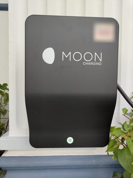 Black Moon Charging wallbox on a white porch column with plants below