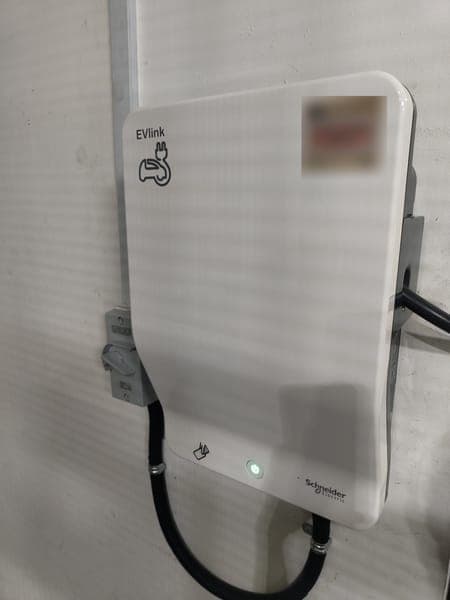 White Schneider EVlink wallbox with a black cable on a white wall
