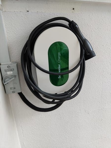 White Schneider Charge wallbox with its cable coiled over the top, beside an isolator