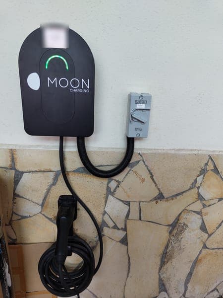 Moon Charging wallbox and isolator above a stone-clad wall, with a holstered plug