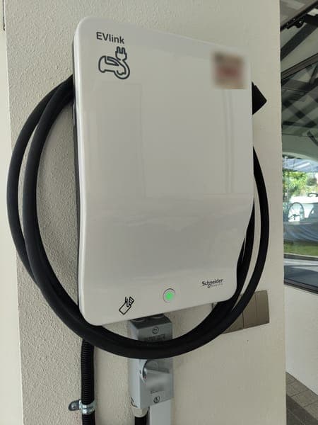 White Schneider EVlink wallbox with a coiled cable on a column in a building car park