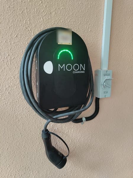 Moon Charging wallbox with a green light, coiled cable and isolator on a textured wall
