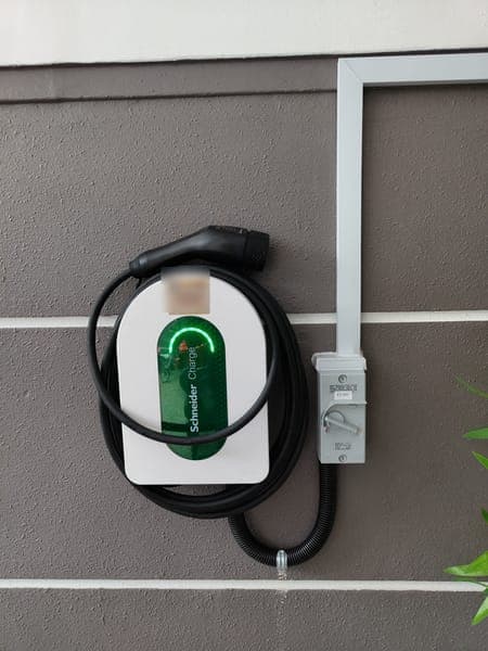 Compact white Schneider Charge wallbox and isolator on a grey striped wall