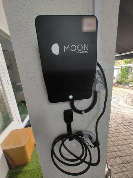Moon Charging wallbox and holstered plug on a porch column beside a paved driveway