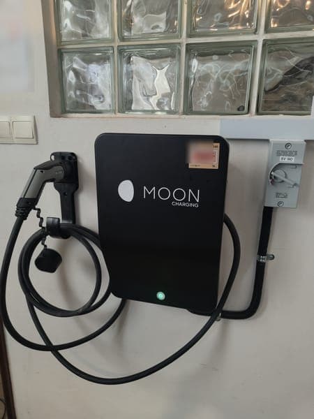 Moon Charging wallbox with a holstered plug below a glass-block window