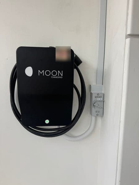 Moon Charging wallbox with a coiled cable beside its isolator on a white wall