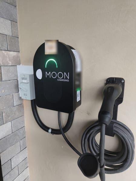 Moon Charging wallbox and holstered plug beside a grey brick-clad wall