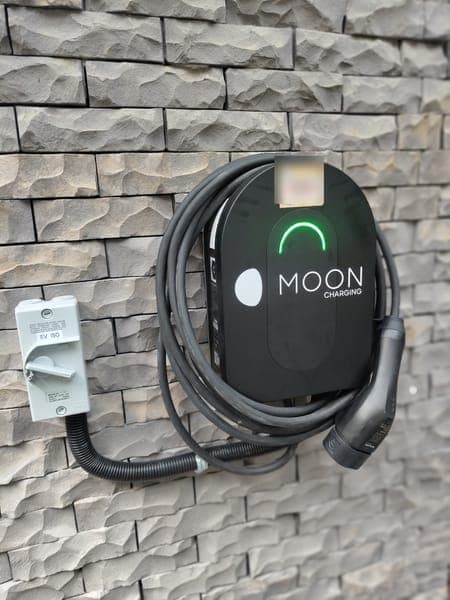 Moon Charging wallbox with a green light on a stone-clad feature wall