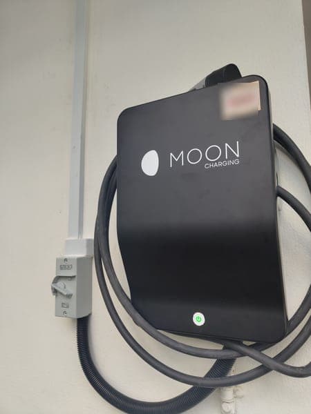 Moon Charging wallbox with a coiled cable on a white porch wall