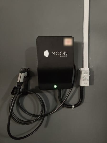 Moon Charging wallbox with a holstered plug on a dark grey wall