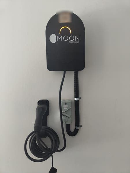 Moon Charging wallbox with an amber light and a holstered plug on a white wall