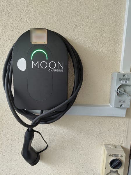 Moon Charging wallbox with a green light and coiled cable on a cream wall