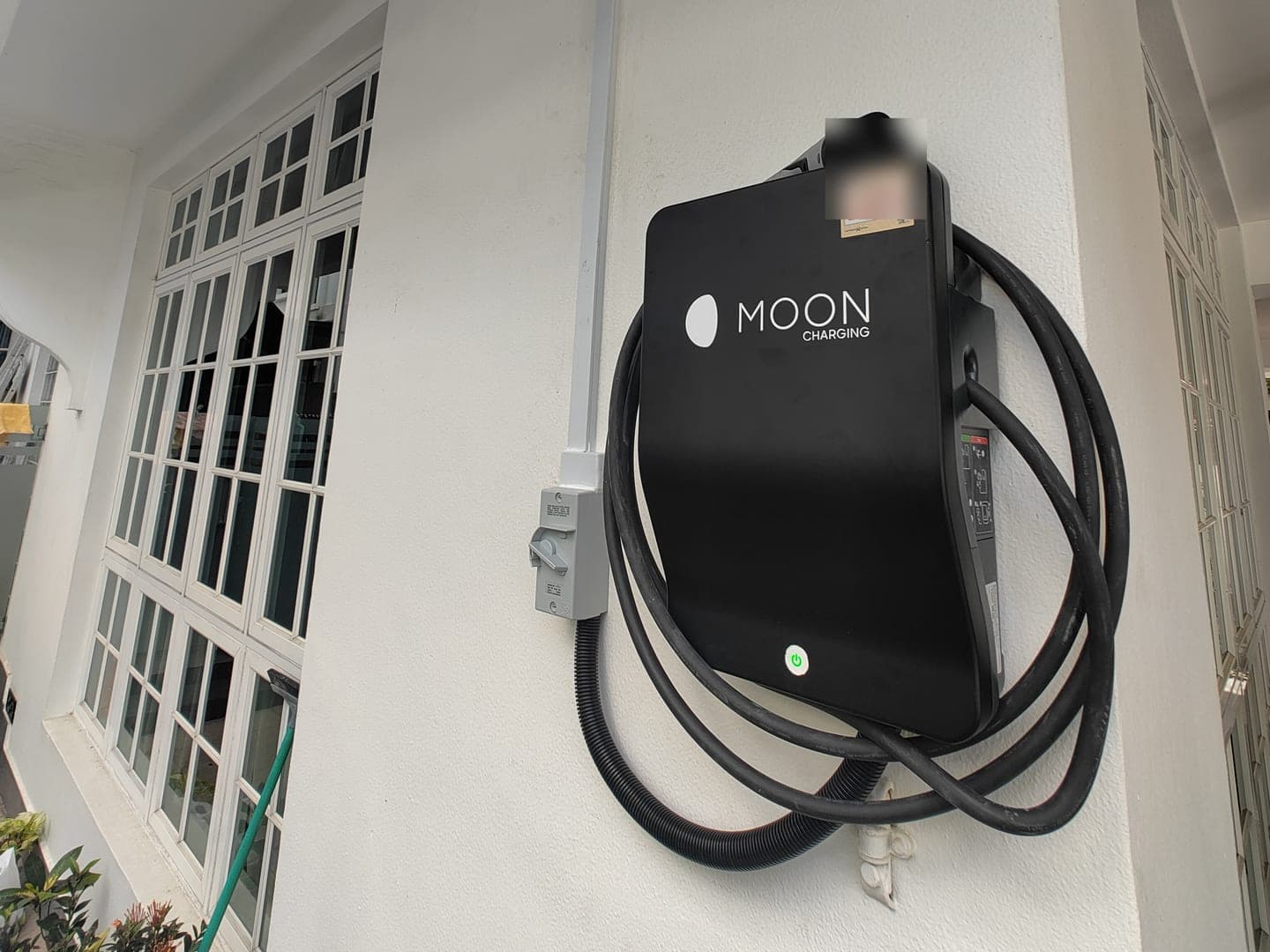 Black Moon Charging wallbox with its isolator on the porch wall of a landed home, beside white French windows