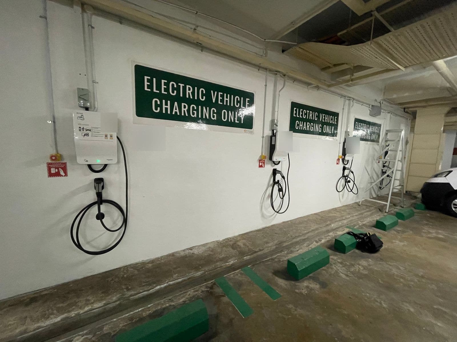 Row of wall-mounted Schneider EVlink chargers under green Electric Vehicle Charging Only signs along the EV lots in the basement car park at The Madeira