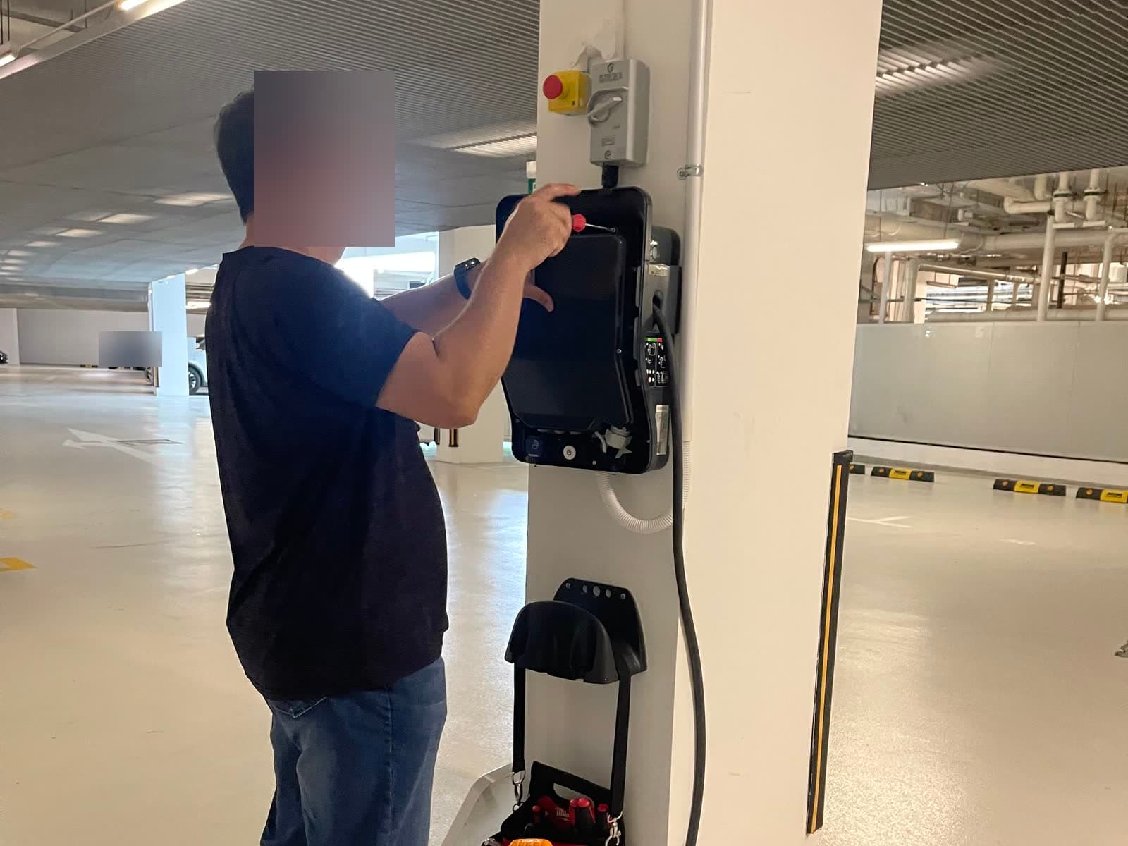 SuperCharge.SG technician servicing an opened wall charger on a car park pillar, with the tool bag hung below
